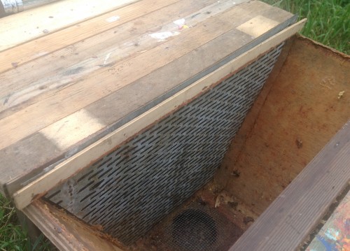 Moerrooster in de lattenkast, op de juiste afstand van de raat gebracht door middel van smalle vullatjes. Je ziet dat het rooster een beetje kiert bij de kastwand. Toch verwacht ik niet dat de moer er tussendoor zal kruipen.