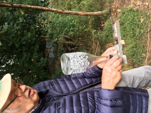 Hier de imkervader met het <br />'antieke' voerapparaatje<br />waarin onscherp nog een honderdtal bijen zitten die de laatste resten<br />suikerwater aan het oplikken zijn.<br />De meeste vlogen terug naar de kast toen ik het toestelletje uit<br />de extra opening van de kast trok.